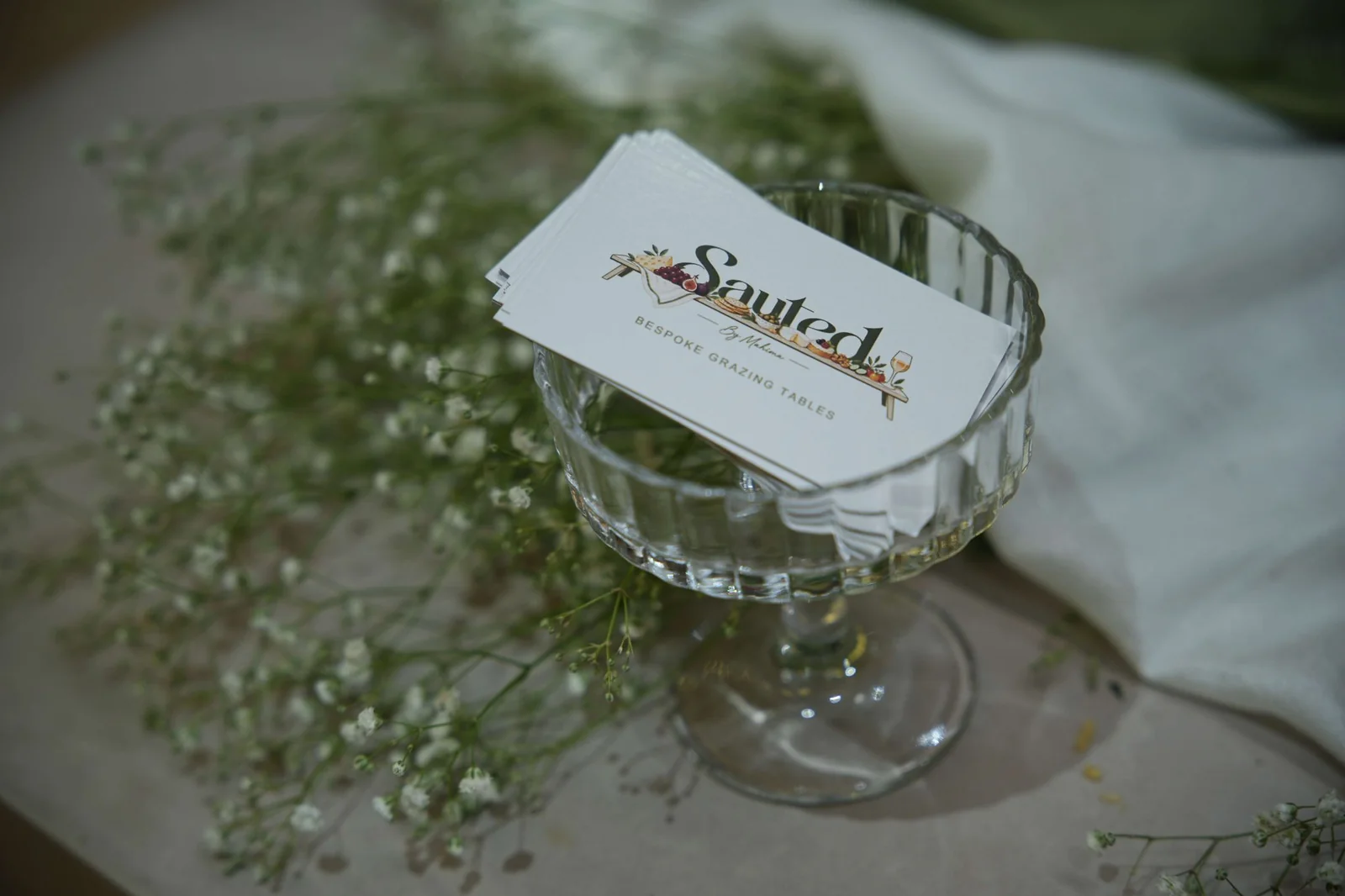 A Sauted card beside glassware and greenery on the table.