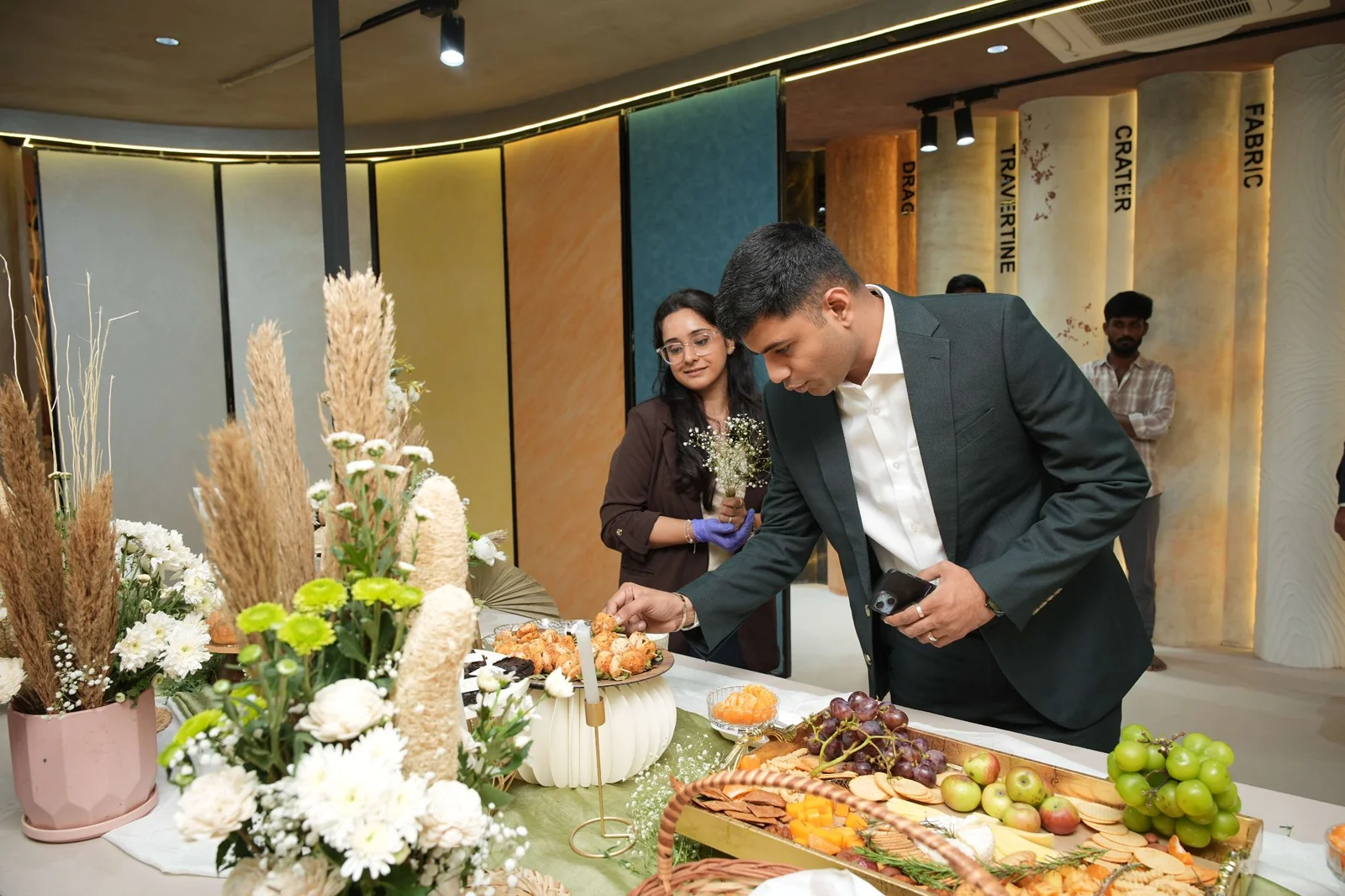 Two guests selecting food beside tall dried foliage and flowers.